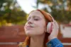 Junge Frau mit roten Haaren hört mit geschlossenen Augen über ihre Kopfhörer Musik oder Podcast