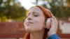 Junge Frau mit roten Haaren hört mit geschlossenen Augen über ihre Kopfhörer Musik oder Podcast