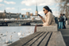 Frau sitzt in Zürich am Wasser und guckt auf ihr Handy
