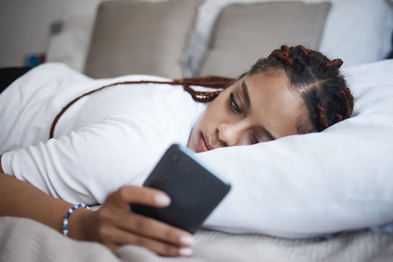 Frau, die auf einem Sofa liegt und auf ihr Handy schaut.