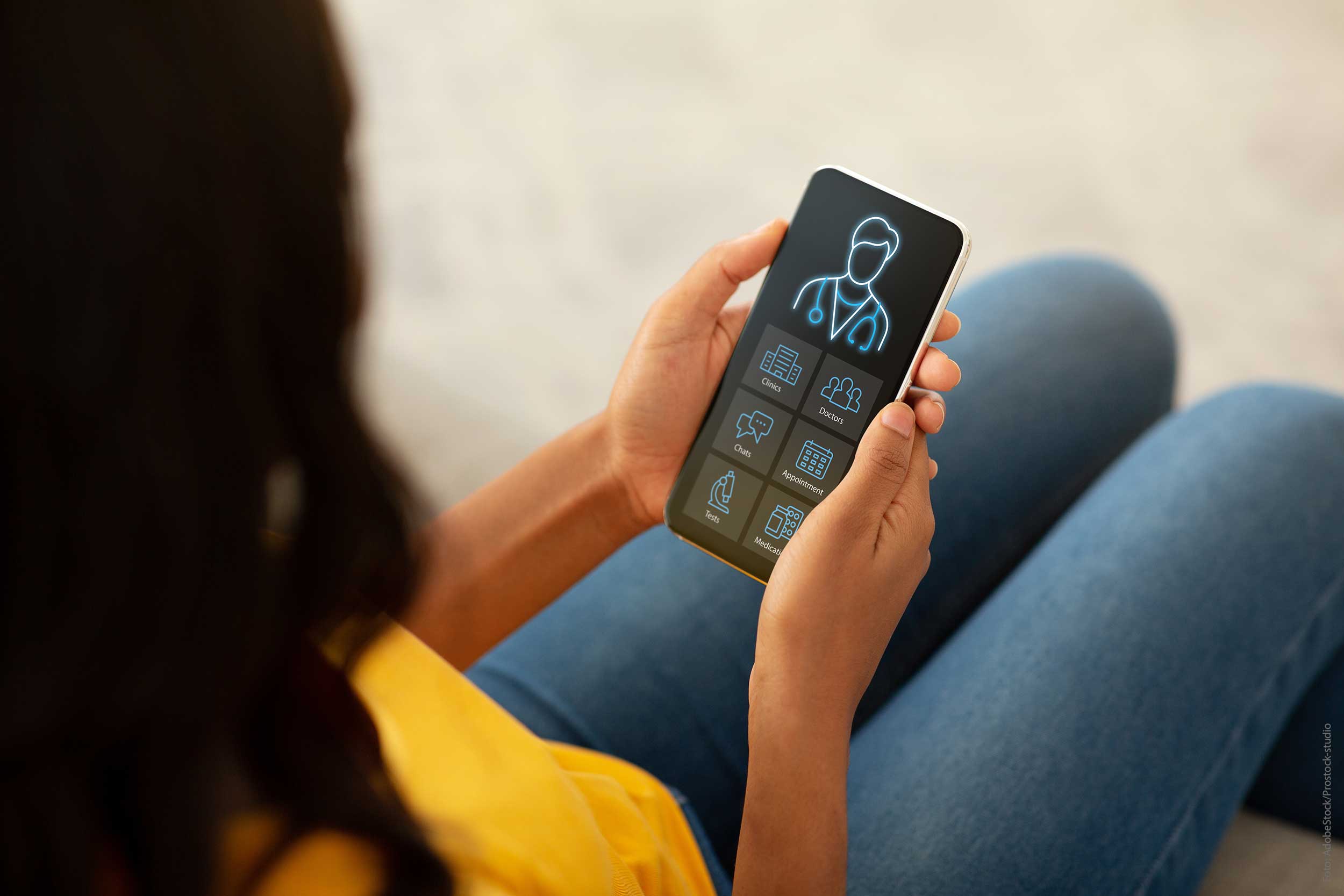 Frau von hinten, die ein Smartphone in der Hand hält. Auf dem Smartphone sind medizinische Symbole.